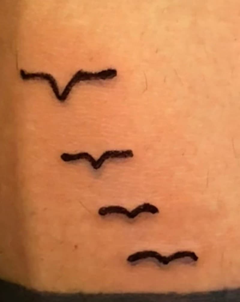 Tatuaje minimalista de pájaros en vuelo, línea fina, en el antebrazo.