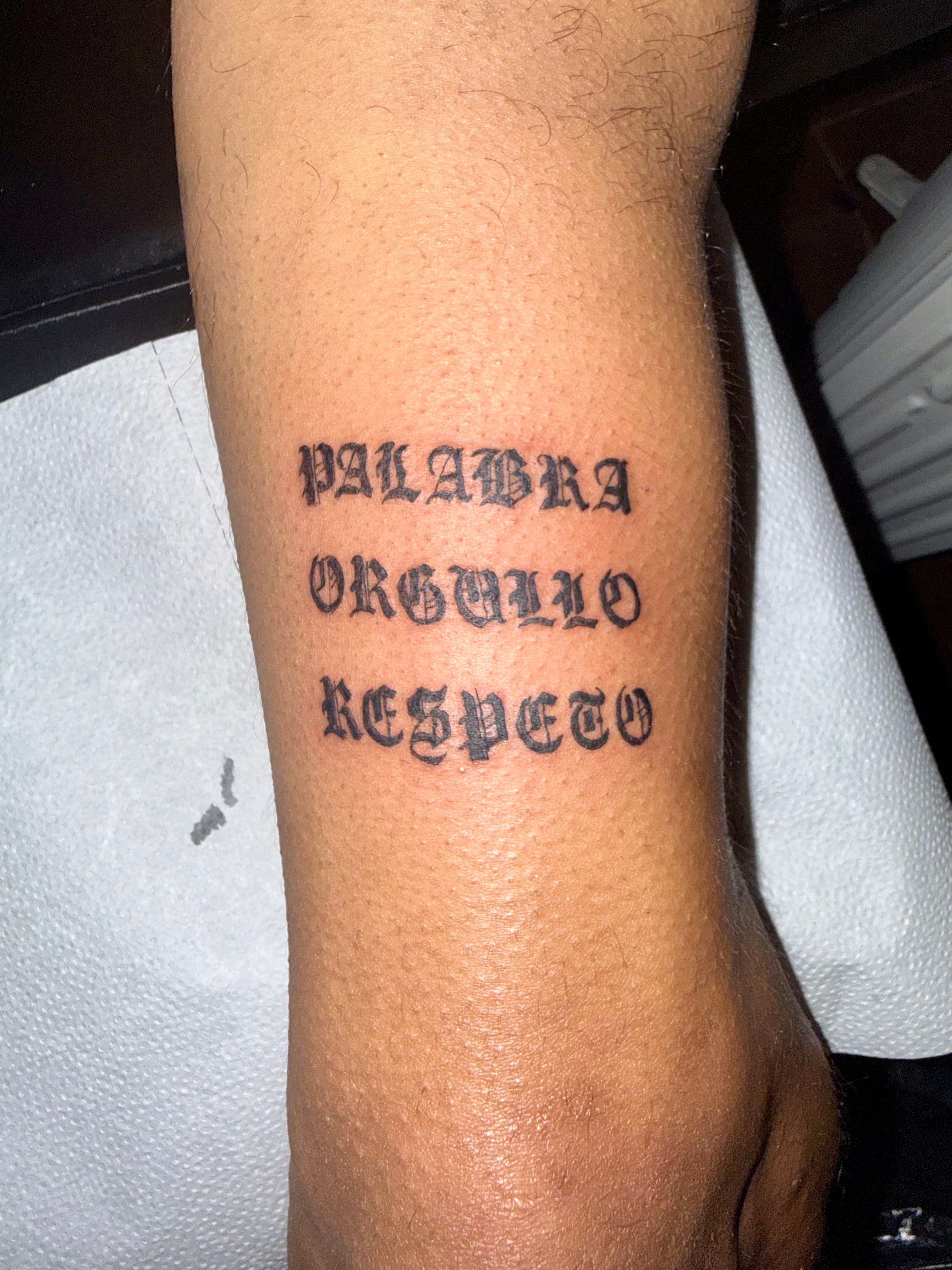 Lettering gótico 'Palabra · Orgullo · Respeto' tatuado en el antebrazo.