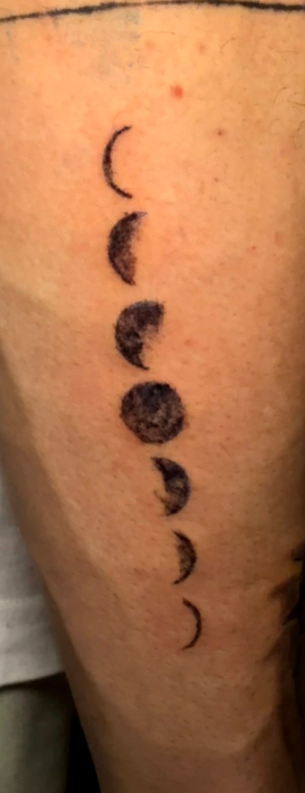 Tatuaje de fases lunares en línea vertical, blackwork, en el antebrazo.